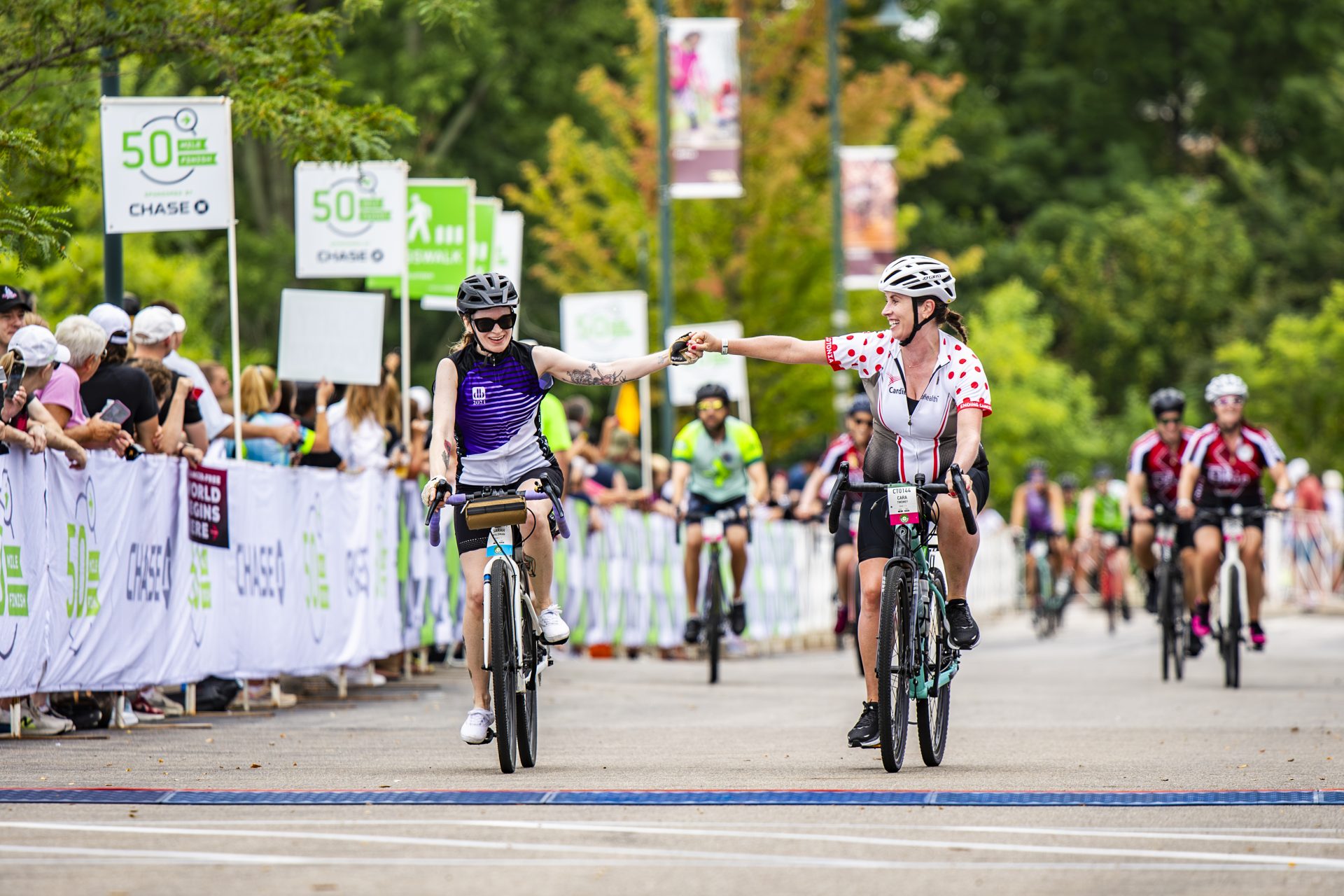Pelotonia2024_Saturday_CEO_1059 2 bike riders for pelotonia fist bumping at the finish line